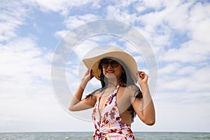 Beautiful young woman posing on the beach with a hat to protect herself from the sun. The woman is enjoying her trip to a paradise