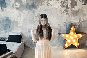 Beautiful young woman posing in bedroom on gray wall background and bright luminous decorative star