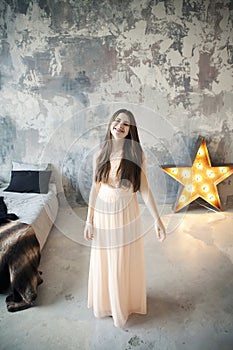 Beautiful young woman posing in bedroom on gray wall background and bright luminous decorative star