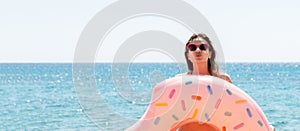 Beautiful young woman is posing with a doughnut inflatable ring and giving a kiss at the sea background