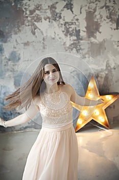 Beautiful young woman posing on gray wall and bright luminous decorative star