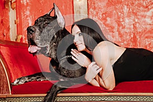 Beautiful young woman posing with her Great Dane dog in the studio in the red room on the couch