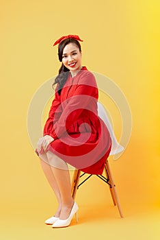 Beautiful young woman posing and looking away with smile while sitting on chair against orange background