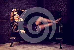 Beautiful young woman posing in stockings and Venetian mask on sofa. Retro glamor vintage woman.