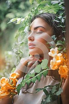 Beautiful young woman posing in Trumpet vine flowers in summer garden. Beauty model girl with Campsis. Enjoying nature