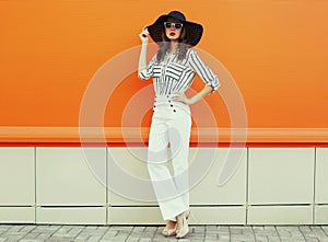 beautiful young woman posing wearing a white striped shirt, black round hat on orange background