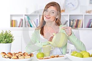 Beautiful young woman pouring tea in cup