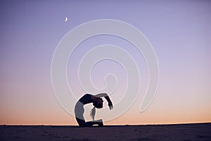 Beautiful young woman practices advanced variation of camel pose - Ustrasana in the desert at night