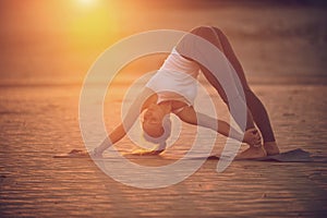Beautiful young woman practices yoga asana Adho Mukha Svanasana - downward facing dog in the desert at sunset