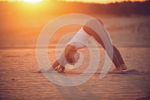 Beautiful young woman practices yoga asana Adho Mukha Svanasana - downward facing dog in the desert at sunset