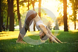 Beautiful young woman practices yoga asana downward facing dog in the park at sunset photo