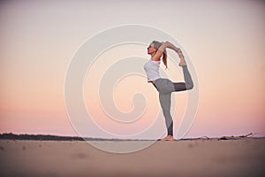 Beautiful young woman practices yoga asana Natarajasana - Lord Of The Dance pose in the desert at sunset