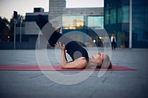 Beautiful young woman practices yoga asana Padma Sarvangasana - shoulderstand lotus pose outdoors against the background of a mode