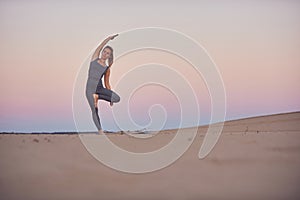 Beautiful young woman practices yoga asana Parshva Vrikshasana - Tree pose in the desert at sunset