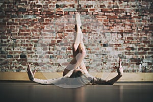 Beautiful young woman practices yoga asana Prasarita Padasana at the yoga studio on a brick wall background. photo