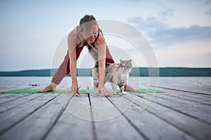 Beautiful young woman practices yoga asana Prasarita Padottanasana on the wooden deck near the lake