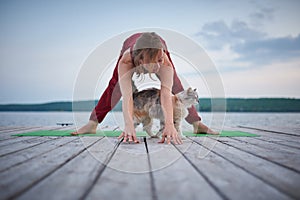 Beautiful young woman practices yoga asana Prasarita Padottanasana on the wooden deck near the lake