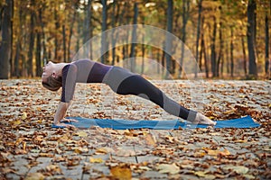 Beautiful young woman practices yoga asana Purvottanasana Upward Plank Pose on the wooden deck in the autumn park.