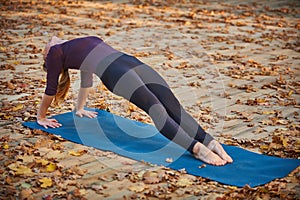 Beautiful young woman practices yoga asana Purvottanasana Upward Plank Pose on the wooden deck in the autumn park.