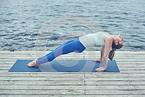 Beautiful young woman practices yoga asana Purvottanasana Upward Plank Pose on the wooden deck near the lake