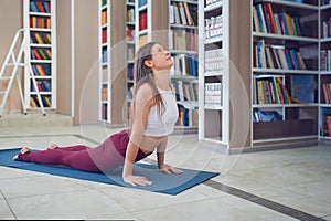 Beautiful young woman practices yoga asana upward facing dog pose in the library