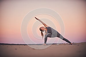 Beautiful young woman practices yoga asana Utthita Parshvakonasana - Extend Side Angle Pose in the desert at sunset photo