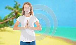 Beautiful young woman practicing yoga in the beach tropical and making namaste mudra