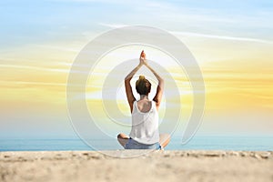 Beautiful young woman practicing yoga near sea at sunrise, back view