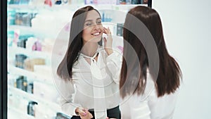 Beautiful young woman preens herself in front of mirror in cosmetic store