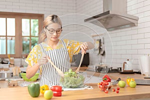 Beautiful young woman is preparing vegetable salad in the kitchen and looking at camera. Healthy Food. Vegan Salad. Diet