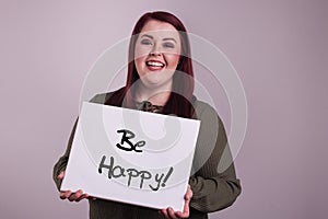 Beautiful young woman presenting a sign that says Be Happy painted on whiteboard