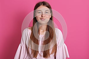 Beautiful young woman puffing out cheeks, having fun making funny face isolated over rosy background, lady with long straight hair