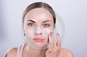 Beautiful young woman puts scrub cream on her face.