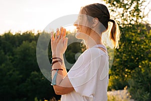 Beautiful young woman putting hands in namaste mudra posture outside in park evening.