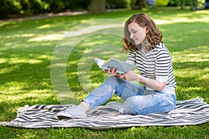 Beautiful young woman read book while relaxation in park at summertime
