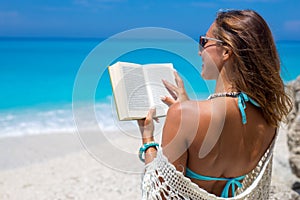 Beautiful young woman reading a book on the beach