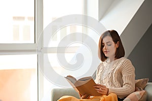 Beautiful young woman reading book at home