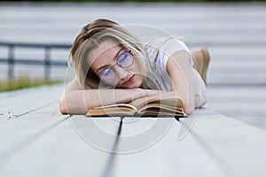 Beautiful young woman reading a book lying on the bench in the park