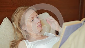 Beautiful young woman reading a sad book in bed