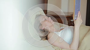 Beautiful young woman reading a sad book in bed