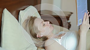 Beautiful young woman reading a sad book in bed