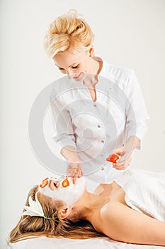 Beautiful young woman receiving fruit mask on a face in beauty salon - indoors