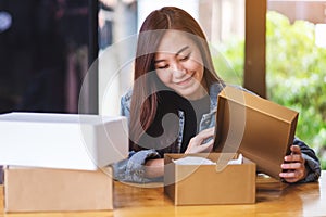 A beautiful young woman receiving and opening a postal parcel box at home for delivery and online shopping concept