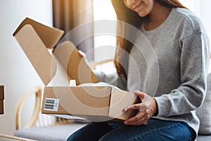 A beautiful young woman receiving and opening a postal parcel box at home for delivery and online shopping concept