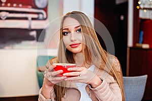 Beautiful young woman with a red cup of coffee at a cafe. Woman drinking hot latte coffee at cozy coffee shop