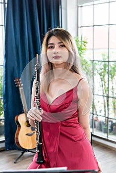 Beautiful young woman in a red dress playing the clarinet .,Classical musician oboe playing