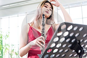 Beautiful young woman in a red dress playing the clarinet .,Classical musician oboe playing