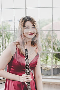 Beautiful young woman in a red dress playing the clarinet .,Classical musician oboe playing