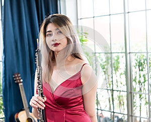 Beautiful young woman in a red dress playing the clarinet .,Classical musician oboe playing