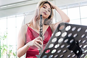 Beautiful young woman in a red dress playing the clarinet .,Classical musician oboe playing